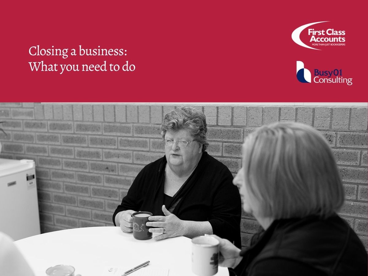 Two women discussing business finances at a table beneath First Class Accounts Ovens & Murray and Busy01 Consulting branding, with the heading “Closing a business: What you need to do”.