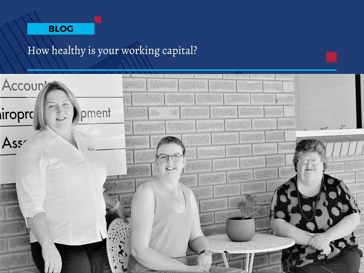Three women from First Class Accounts Ovens and Murray sitting and standing outside an office building, smiling at the camera with a brick wall and business signage in the background.