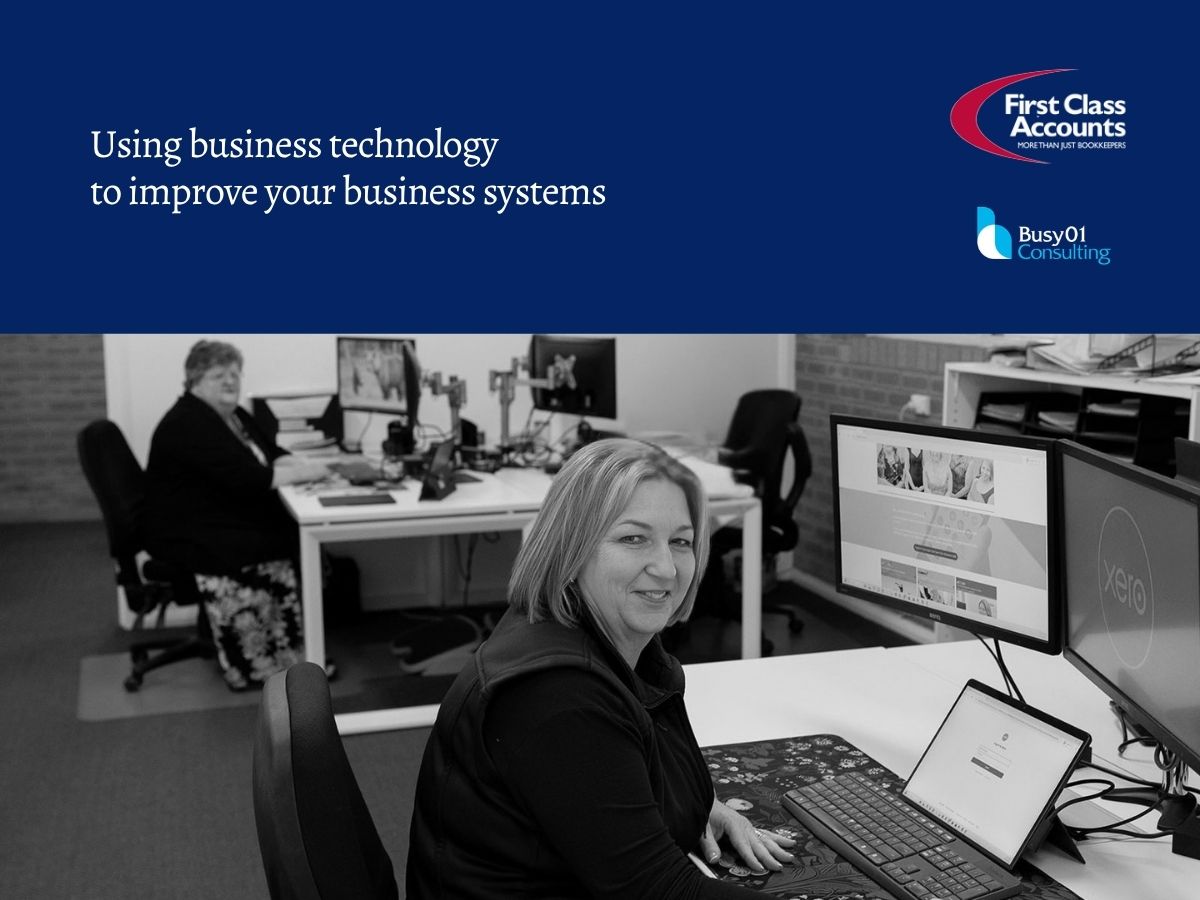 First Class Accounts Ovens & Murray and Busy01 Consulting graphic titled “Using business technology to improve your business systems”, featuring a black and white office photo of a woman working at a desk with a laptop and dual monitors, with another team member working in the background.