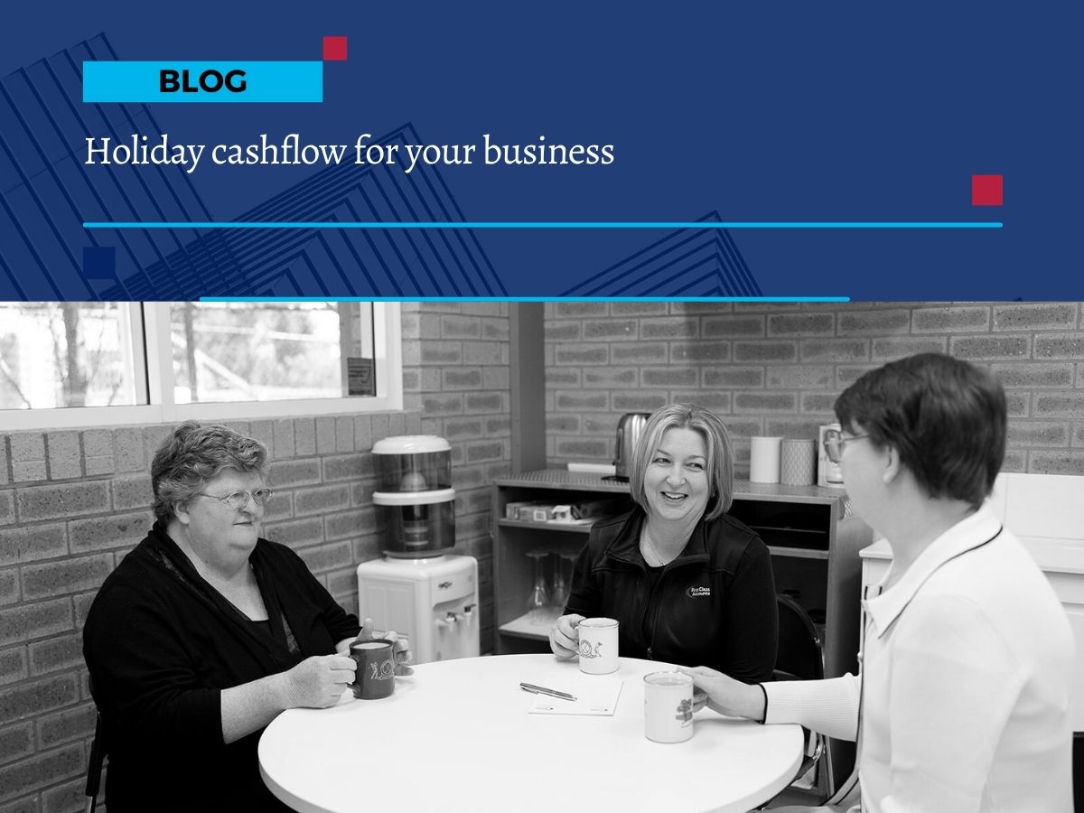 Three First Class Accounts Ovens & Murray team members sitting at a round table in the office kitchen, talking and smiling while holding coffee mugs.
