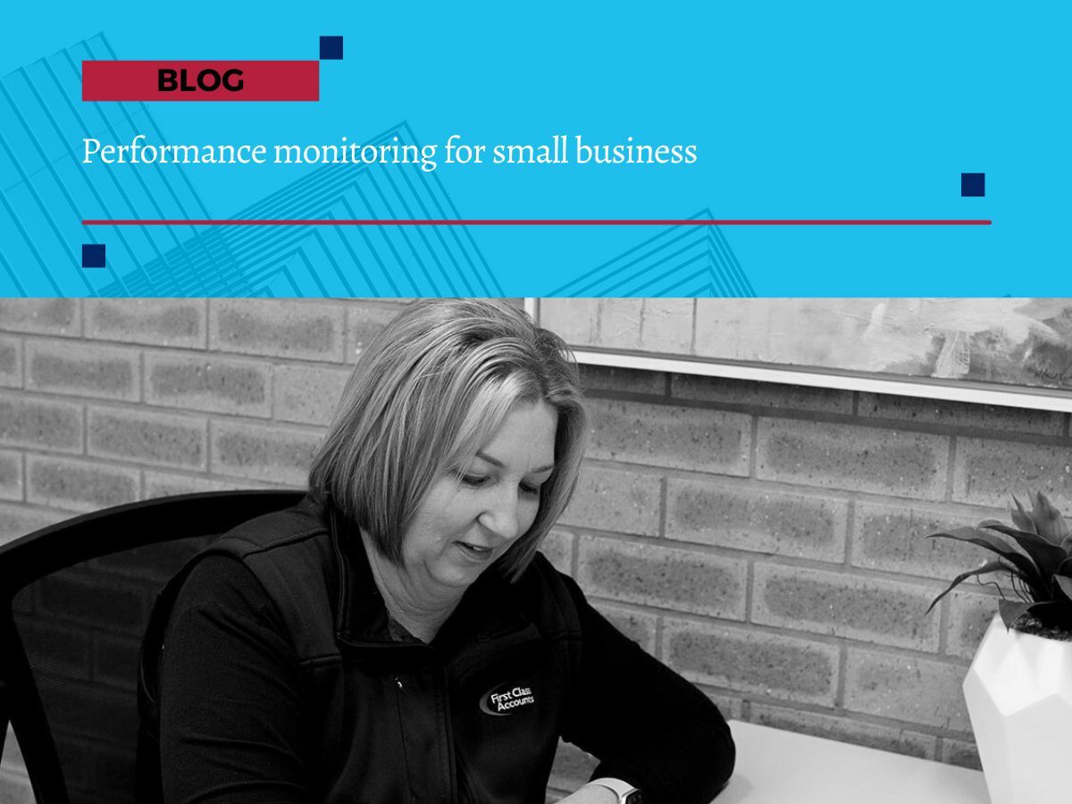 Performance monitoring for small business First Class Accounts Ovens & Murray bookkeeper working at her desk, reviewing client financial data. The image features a woman with shoulder-length blonde hair, wearing a branded First Class Accounts vest, seated against a brick wall. She is focused on her work, representing the reliability and professionalism of bookkeeping and payroll services in Albury Wodonga.