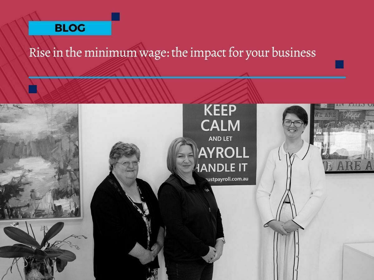 Minimum wage increase impact Three women from First Class Accounts Ovens & Murray standing in front of a sign that reads